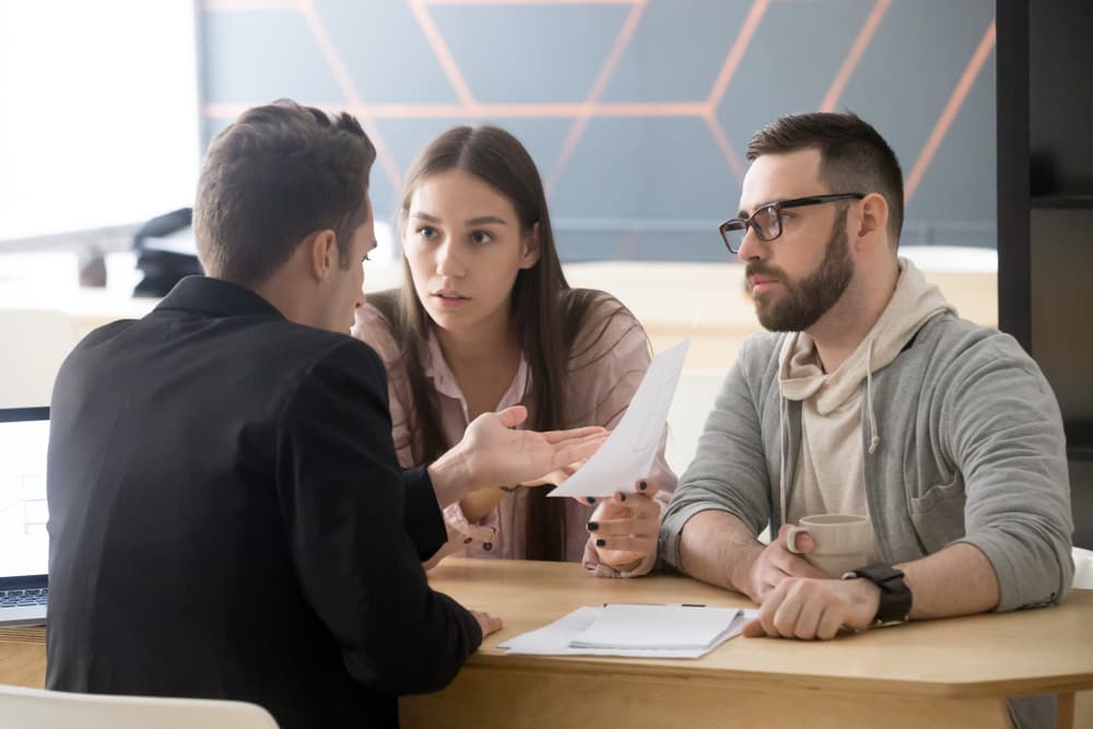 Unhappy young couple discussing legal issues with a lawyer, expressing frustration over a bad contract.