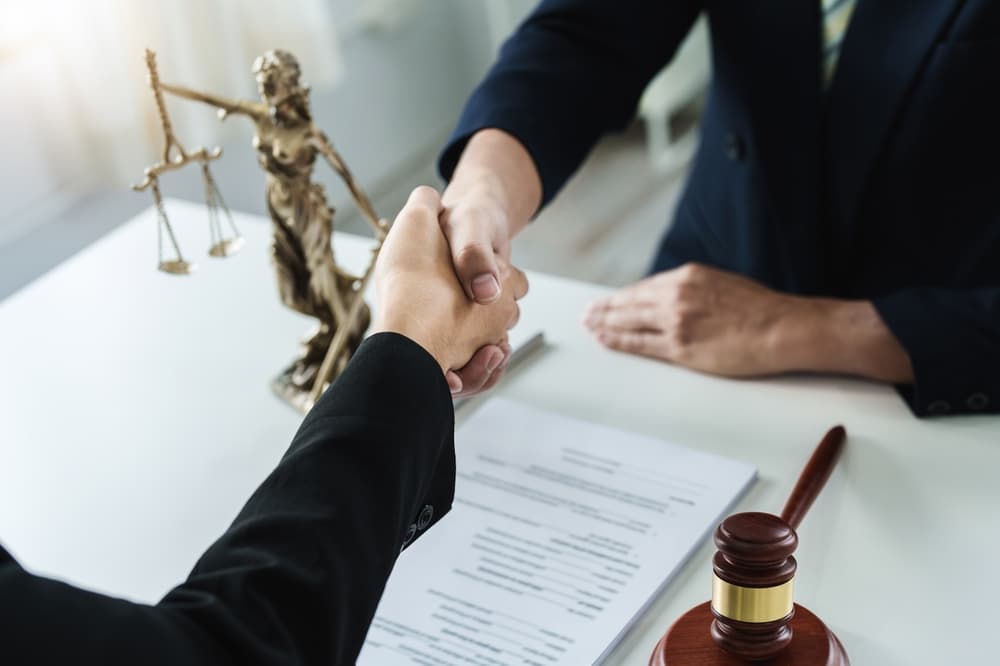 Lawyer shaking hands with client to accept offer for legal representation in court case.