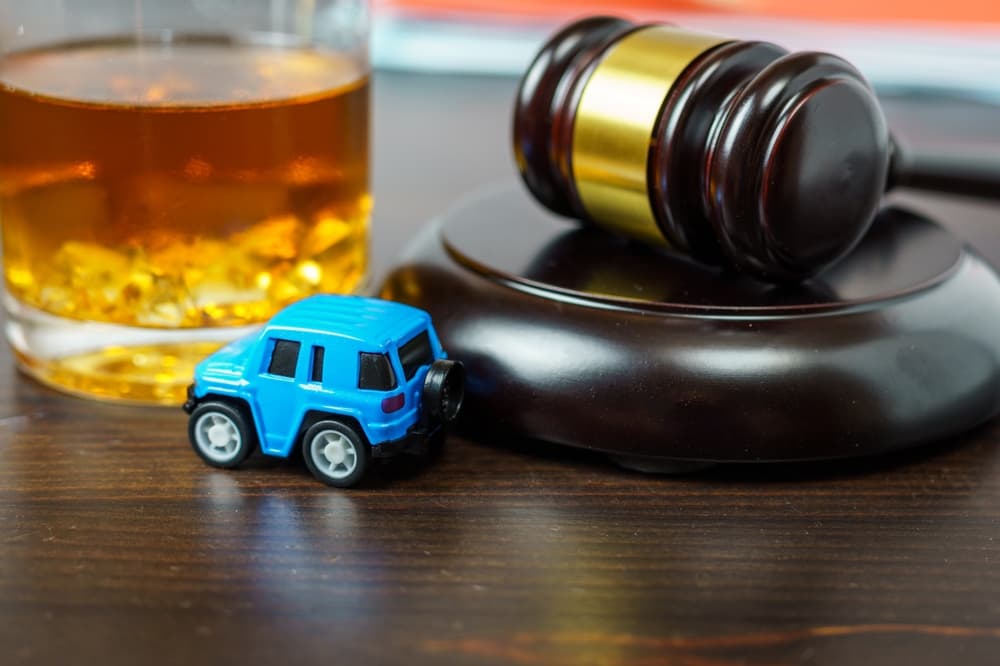 Judge's gavel on a table, glass of whiskey and miniature car. 
