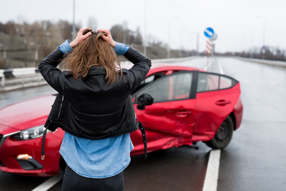 Woman stands near a damaged car after an accident.