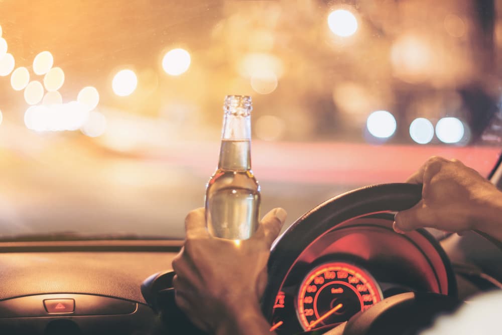 A young man drives a car with a bottle of beer.