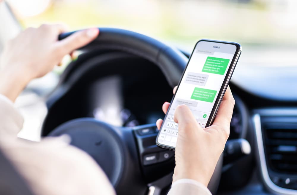Person texting on phone while driving, ignoring the road, potentially unsafe.
