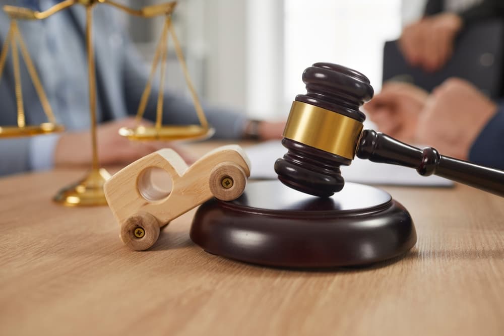 Wooden gavel and scales of justice with toy car on desk.