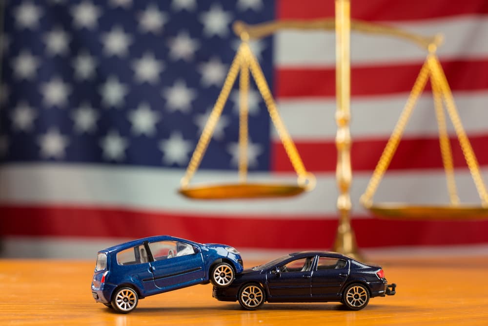 Toy cars in collision before American flag and justice scales.