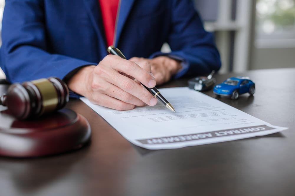 Insurance agent signs documents for auto coverage, gavel and toy car nearby.