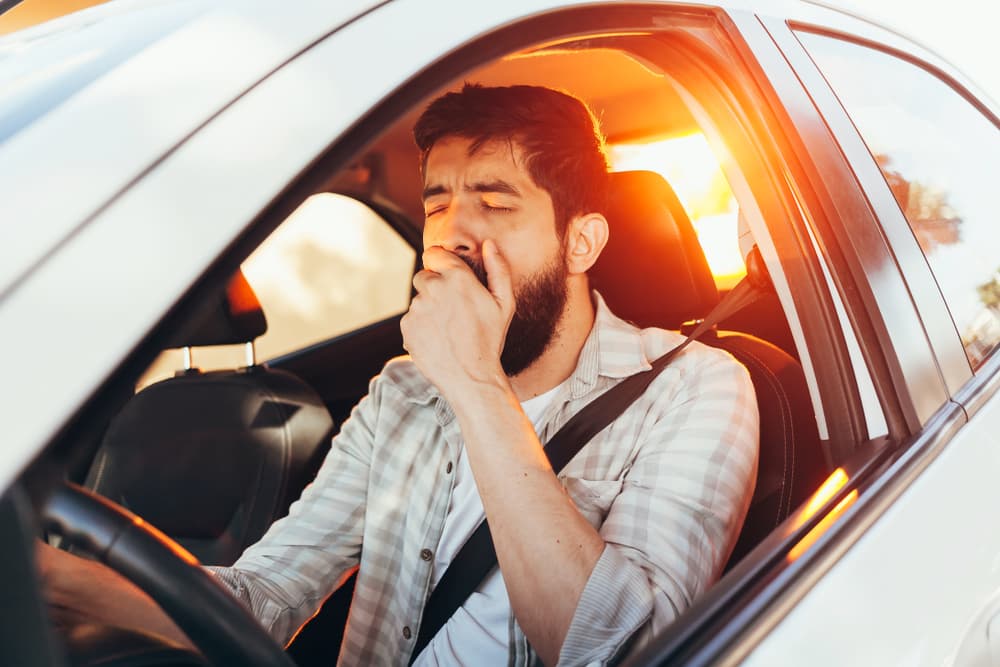 Tired man yawning while driving his car.